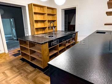 Detail kuchyňské pracovní desky ze žuly Nero Assoluto Zimbabwe (trattato), v pozadí varný ostrůvek ze stejného materiálu. Zakázková výroba TONE OF STONE. Detail kuchyňské pracovní desky ze žuly Nero Assoluto Zimbabwe (trattato), v pozadí varný ostrůvek ze stejného materiálu. Zakázková výroba TONE OF STONE.